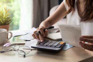 Mulher calculando RPV do INSS com calculadora e documentos.
